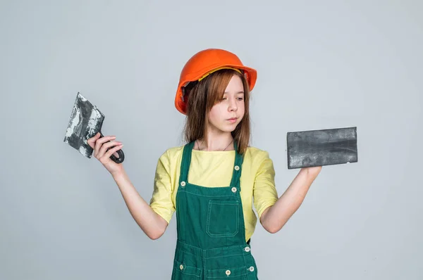 Kezdjük. felújítás és javítás. munkaeszközzel. Tini lány sisakban és boilersuit spatulával. A gyerek keménykalapot visel. Gyereképítő az építkezésen. Munkás mérnök. építész műhelyben — Stock Fotó