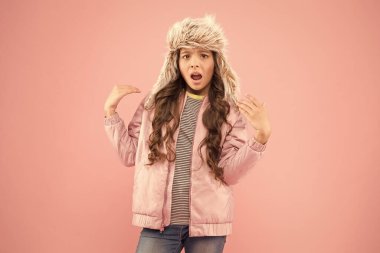 Narsist modacı. Uzun saçlı çocuk yumuşak kürk şapkası yumuşaklığın tadını çıkarır. Kış moda konsepti. Soğuk hava için sıcak şapka. Sahte kürk trendi. Uzun kıvırcık saçlı kız kürk şapkalı kulaklık takıyor pembe arka plan