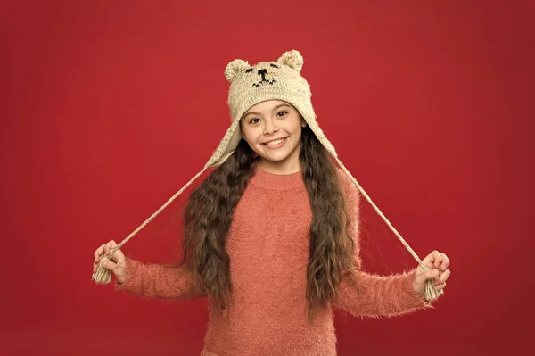 Зимове вбрання. Маленька дитина носить в'язаний капелюх. Залишайтеся в теплі. Маленька дівчинка зимовий модний аксесуар. Маленька дитина з довгим волоссям носить капелюх червоний фон. Милі моделі насолоджуються зимовим стилем. Чарівний маленький ведмідь — стокове фото