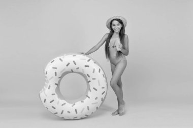 Bronzlaşmak ve tatilin tadını çıkarmak. Mayo ve hasır şapkalı neşeli küçük kız. Havuz sahili eğlencesi. Solaryum ürünü olan bir çocuk. Küçük güzellik. Mutlu çocuk ve lastik yüzük. Yaz tatili aktivitesi. bronzlaşma yağı