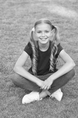 Küçük tatlı kız at kuyruğu saç stili yeşil çimlerde dinleniyor, iyimser bir kavram.