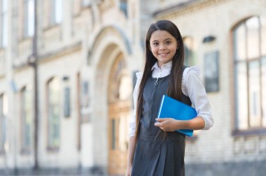 Okullu küçük mutlu çocuk üniforma giyiyor kütüphane kitabını dışarıda tutuyor, ders çalışıyor.