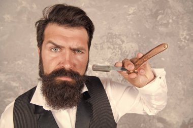 Sakallı ve şık. Retro ve klasik moda. Saç ve sakal bakımı. Kendine güvenen ve yakışıklı vahşi bir adam. Erkek sabah bakımı. Kişisel yüz bakımı. Tıraş eden adamın jileti var. Erkekler için kuaför salonu