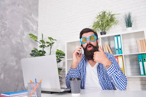 Yllättynyt hipster viileä lasit osoittavat peukalot ylös käsi ele puhuu matkapuhelimeen modernissa toimistossa, hyväksyntä — kuvapankkivalokuva