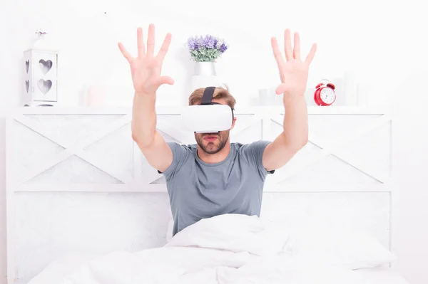 La migliore esperienza VR. Un bel ragazzo con le cuffie VR a letto. Uomo caucasico che usa occhiali VR in camera da letto. Rendering immersivo in VR — Foto Stock