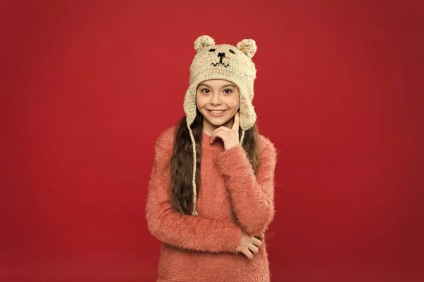 귀여운 작은 곰이야. 겨울 의류. 꼬마 애는 뜨개질 모자를 쓰고 있어. 따뜻하게 있어. 어린 소녀의 겨울 패션 액세서리. 어린이의 긴 머리는 모자를 빨간 배경으로 하고 있다. 귀여운 모델 겨울을 즐기다 — 스톡 사진
