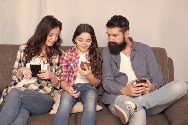 Oyun uygulaması oynat. Çevrimiçi aile. Anne baba ve kızı kanepede dinleniyor. Aile hafta sonunu internette geçiriyor. Küçük bir kız çocuğu, ailesine karşı akıllı telefon kullanıyor. İnternette aile sörfü. Aile eğlencesi.