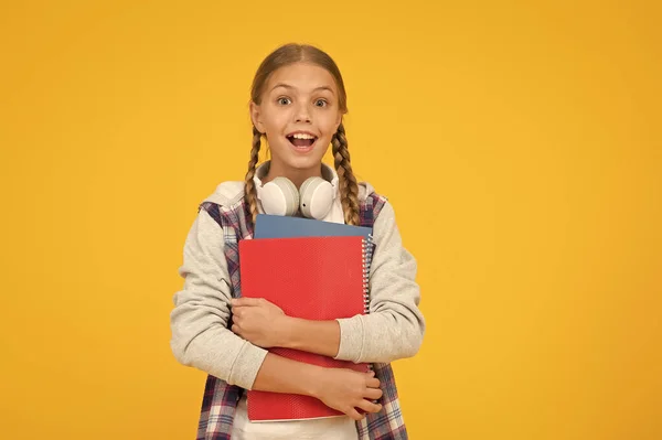 Pequeño niño feliz en auriculares con bloc de notas. niño listo para aprender el tema. de vuelta a la escuela. Clases de estudio para examen. siente la gran sorpresa. Día del conocimiento. sorprendido alumno amarillo fondo, espacio de copia — Foto de Stock