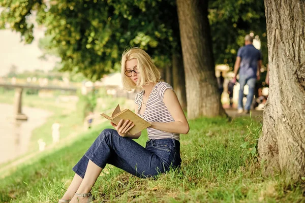 Література для літніх канікул. Літня відпустка. Студентський розумний ботанік сидить на зеленій траві і читає книгу. Дівчина розслабляється на березі річки після робочого дня. Розслабтеся і захоплюйтеся. Жінка мріє про відпустку — стокове фото