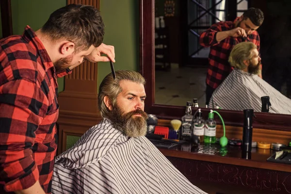 Професійний перукар у перукарні. Клієнт Гіпстера стрижеться. Перукар і клієнт. Барбер працює в перукарні для бородатого чоловіка. Хлопець з довгим світлим волоссям. — стокове фото
