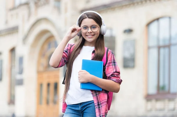 헤드폰을 끼고 학교에 있는 행복 한 아이는 밖에서 안경을 고칠 수있고, 오디오 강의를 들을 수있습니다. — 스톡 사진