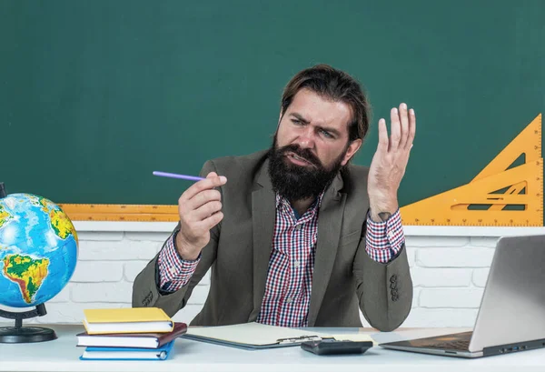 Sin tinta. hombre confundido con el trabajo de barba en la computadora. estudiar en línea. educación informal. estudiante masculino se sienta en el aula de la escuela en la lección con pizarra. aprobar el examen. aprender el tema —  Fotos de Stock