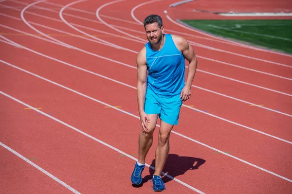 Duele demasiado. trauma masculino. deportista atleta flexionar los músculos y amasar una articulación. hombre tiene lesión después del ejercicio en el estadio. gimnasio gimnasio al aire libre. musculoso atlético con moretones. entrenamiento deportivo — Foto de Stock