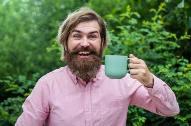 Sakallı adam içecek içiyor. Sakallı olgun bir hippi kahve içer. Kafkasyalı vahşi hippi elinde çay fincanı tutuyor. Erkek mükemmel sabah. Tişörtlü mutlu iş adamı.