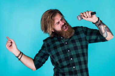 Mikrofonlu erkek şarkıcı. Karaoke konsepti. Kareli gömlekli sakallı adam şarkı söylüyor. Sıradan bir adam şarkı söylerken insani duygularını ifade eder. Mikrofonlu duygusal hipster. Meleklerin dili.