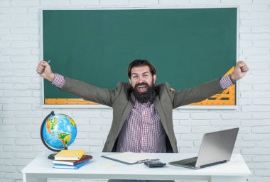 Kostümlü olgun sakallı adam öğretmen. Sınıfta coğrafya haritası ve tatille otur.