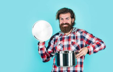 Havalı saç stili olan şık sakallı adam. Kareli gömlek tutacağı takıyor, yemek yapıyor.