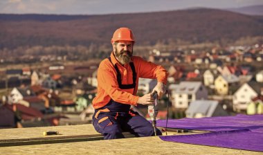 Asıl konu güvenlik. Çatı tamircisi. İnşaat endüstrisi ve su geçirmezlik. İnşaat alanındaki binanın çatı yapısında çalışan bir çatı ustası. Çatı ustası güvenlik üniforması denetimi giyiyor.