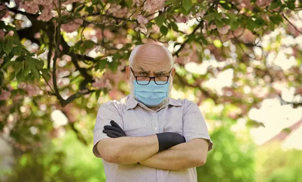 Ernstige opzichter. Lentegenot. Beperkt sakura park. park is gesloten voor quarantaine vanwege coronavirus. senior man met masker en handschoenen. sakura bloesem boom in het park. coronavirus covid19 — Stockfoto