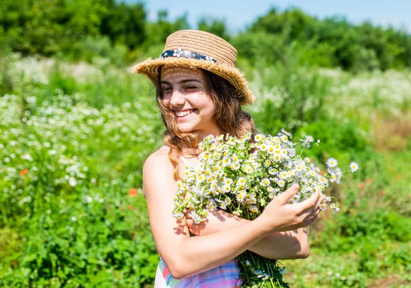 Happy kid smile in sun hat with romomile flower bunch on sunny landscape vacation in countryside summertime, summer — стоковое фото