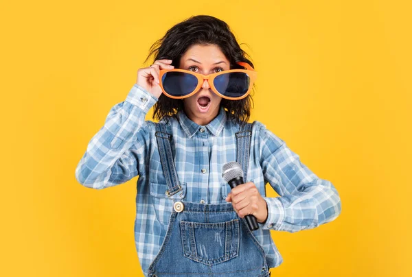 Canto femminile alla musica. donna felice cantare canzone in microfono. cantante ragazza in camicia a scacchi e jeans. Divertente frequentatore di feste. bellezza attraente con microfono. esprimere emozioni umane. ha colpito una nota alta — Foto Stock