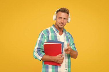 Yakışıklı üniversite hocası işaret ediyor. Yetişkin öğrenci not defterini tutuyor. Kulaklıklı klasörlü adam. Online eğitim. Adam kitap okurken not almak için elinde kitap tutuyor. Not defterine yazalım.