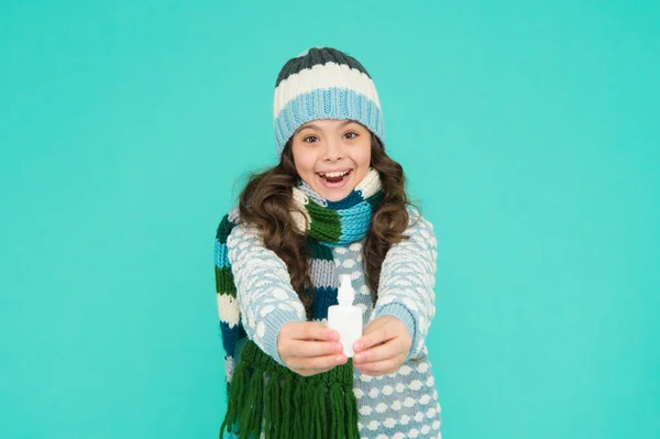 Cheerful kid girl free stuffy nose with nasal drops in knitwear on blue background, coronavirus — Foto Stock