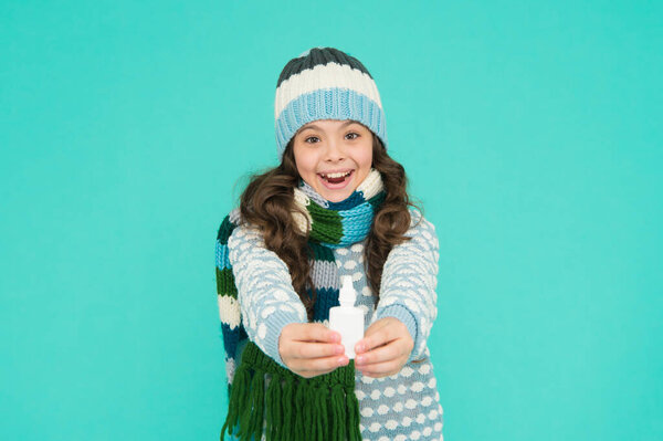 cheerful kid girl free stuffy nose with nasal drops in knitwear on blue background, coronavirus