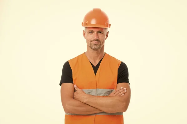 A segurança é o ponto principal. Homem chapéu duro protetor e uniforme fundo branco. Trabalhador construtor confiante olhando câmera. Conceito de equipamento de proteção. Construtor cruzou o peito das mãos. Forte construtor bonito — Fotografia de Stock