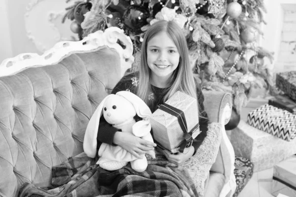 Traumspielzeug. Kleine Mädchen halten Kaninchenspielzeug und Geschenkbox. Kleine Kinder spielen mit Stofftieren. Kleines Kind glücklich lächelnd mit Geschenk. Bestes Weihnachtsspielzeug. Kleines Mädchen mit süßem Hasen am Weihnachtsbaum — Stockfoto