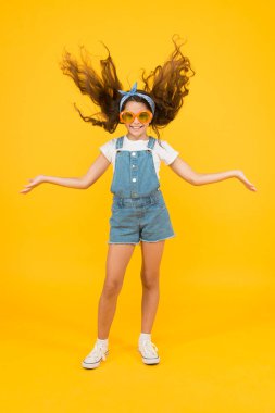 Ne ses ama. Retro çocuk uzun saçı. Küçük bir kız güneş gözlüğü takıyor. Mutlu çocukluk. Güzel bir yaz tatili. Haidresser kuaför konsepti. Bahar çocuğu modası. Neşeli küçük kız sarı arka plan