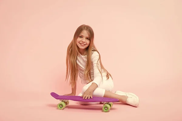 女の子はペニーボードピンクの背景で楽しんでいます。子供の愛らしい子供の長い髪はペニーボードに乗ることを崇拝する。幸せな子供時代。ペニーボードに乗ってトリックを行う。女の子はスケートボードに乗るのが好きです。アクティブなライフスタイル — ストック写真