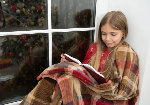 Волшебный дух Рождества. Маленькой девочке нравится читать Рождественскую историю. Маленький читатель, завернутый в клетку, сидит на подоконнике. Маленький ребенок читал книгу в канун Рождества. Моя любимая рождественская книга — стоковое фото