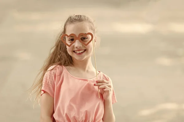 Complimenti per San Valentino. Divertente bambina che indossa oggetti di scena a forma di cuore sul bastone. Piccolo bambino felice che guarda attraverso occhiali puntelli. Ragazzo carino sorridente con oggetti di scena di partito di fantasia — Foto Stock