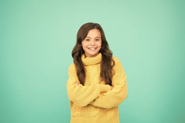 Moda senin kadar eşsiz. Mutlu çocukluk. Uzun esmer saçlı küçük bir kız. Çocuk sıradan kış modası tarzında. Küçük kızın saf güzelliği. Çocuklar için örgü örüyorum. Mavi arka planda küçük bir kız