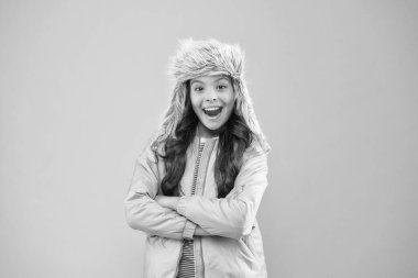 Fotoğraf için poz veriyorum. Sonbahar tarzı. Çocukluk aktivitesi. Çocuk modası. Kız hipster gibi görünüyor. Tüylü kulaklıklı şapka aksesuarı. Küçük kız kış şapkası. Soğuk mevsim için sıcak kıyafetler. Mutlu çocuk pembe arka planı