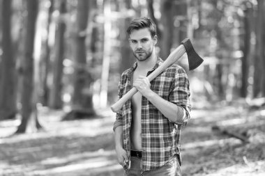 Tıraşsız, ekose gömlekli, kot pantolonlu yakışıklı adam yaz ormanlarında baltayı taşır doğal manzara, oduncu.