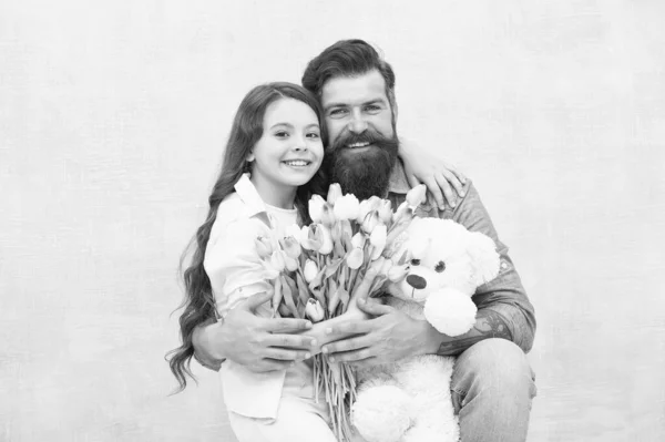 Fantastisk present till den lilla. Trevlig familjesemester. Små barn och skäggig man håller blommor och leksak. En liten dotter kramar far. Gåvobutik. Leksaksaffären. Blomsteraffär. Födelsedagspresent — Stockfoto