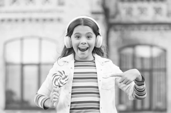 Chica auriculares inalámbricos comen caramelos piruleta, dulce concepto de la infancia — Foto de Stock