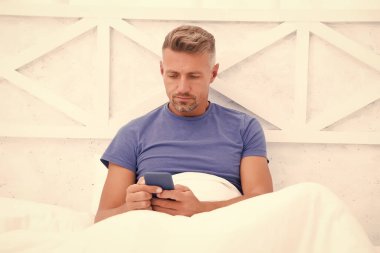 Kendini izole et ve karantina altına al. Evde kal. - Günaydın. Çevrimiçi iletişim. Olgun bir adam yatakta cep telefonu kullanır. Mobil iletişim. Hücresel iletişim. İletişim teknolojisi. Modern hayat