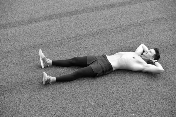 Fitt fiatalember, aki edzés után pihen. Lazíts a jóga után. Az elme és a test harmóniában. Egészséges és egészséges. Egy félmeztelen fickó fekszik a zöld füvön. Ideje pihenni. kikapcsolódásra van szükségem. — Stock Fotó