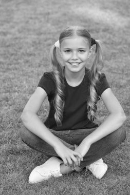 Küçük tatlı kız at kuyruğu saç stili yeşil çimlerde rahatlıyor, tasasız çocukluk konsepti