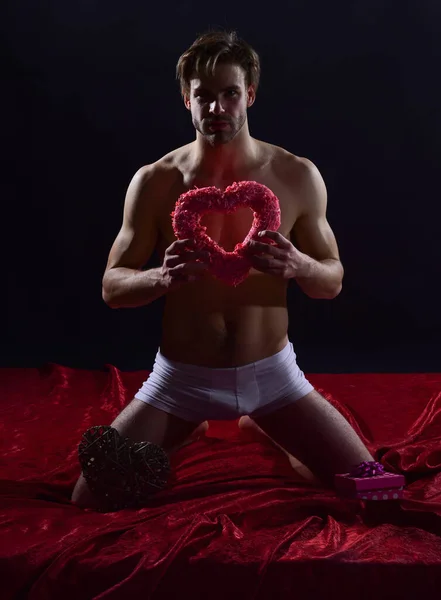 Sexy macho chico con muscular cuerpo desgaste pantalones celebrar corazón forma decoración para San Valentín día, potencia — Foto de Stock