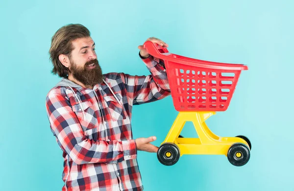 Dia de compras bem sucedido. Comprador masculino com carrinho de compras. O tipo barbudo de camisa quadriculada compra. homem brutal sem barba com barba. comprar produtos no shopping. deveres cotidianos e rotina — Fotografia de Stock