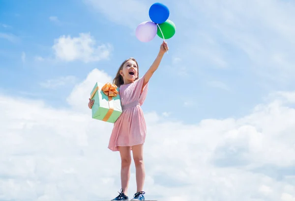 Vrijheid. mooi tienermeisje met kistje. Kindermode stijl. vrouwelijke natuurlijke schoonheid. Gelukkige jeugd. schattig kind op de achtergrond met ballonnen. het voorjaarsweer. zomervakantie en vakantie — Stockfoto