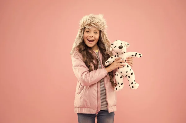 Bij de kinderwinkel. gelukkig kind roze achtergrond. koude seizoen in warme kleding accessoire. Klein meisje Dalmatian hondenspeelgoed. Kindermode. Hipster meisje bont winter oorflap hoed. herfst stijl. Jeugdgeluk — Stockfoto