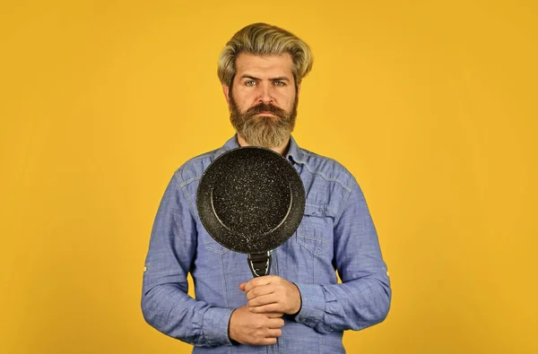 Repas de friture. Parfait pour faire des crêpes. Vases de cuisson en fonte émaillée. Des ustensiles de cuisine. Poêle antiadhésive surface en porcelaine. Un homme tient la poêle. Cuisiner des aliments sains. hipster barbu préparer le petit déjeuner — Photo