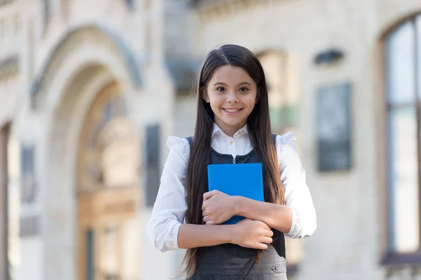 Criança pequena feliz com aparência escolar usar uniforme segurando livro de biblioteca ao ar livre, conhecimento — Fotografia de Stock