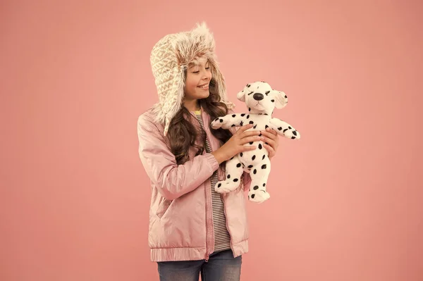 Ik voel me speels. herfst stijl. Jeugdgeluk. Kindermode. Hipster meisje bont winter oorflap hoed. koude seizoen in warme kleding accessoire. gelukkig kind roze achtergrond. klein meisje dalmatian hond speelgoed — Stockfoto