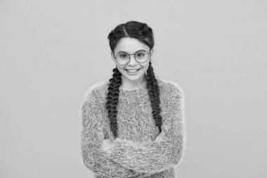 Göz muayenesi zamanı geldi. Gözlük takıyor çünkü gözleri iyi görmüyor. Gözlüklü mutlu kız portresi. Havalı saç stili ile gülümseyen kız. Zeki çocuk sarı arka planda. Pozitif duygular